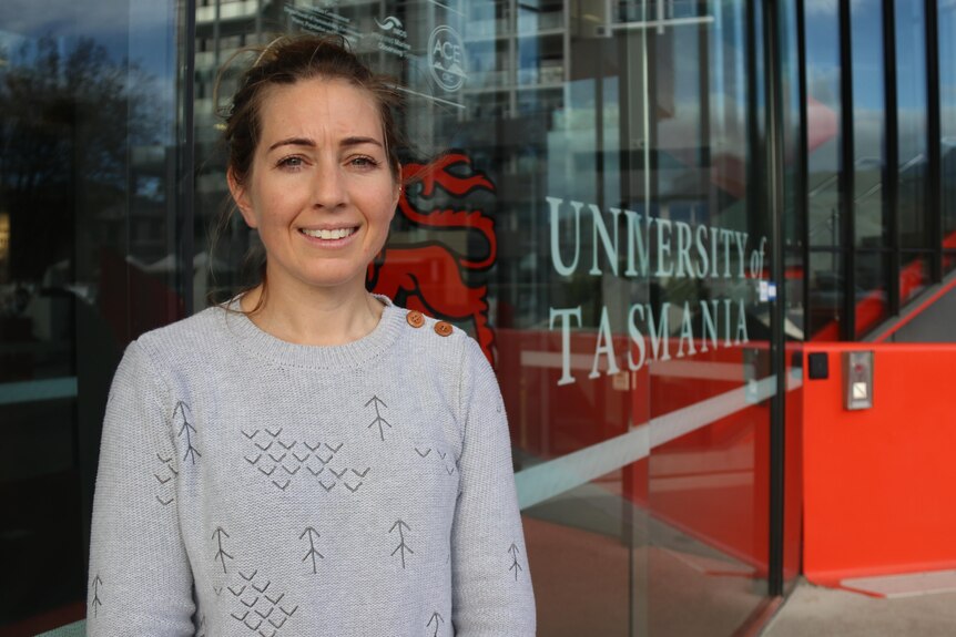 A woman stands in front of a glass window with the words University of Tasmania