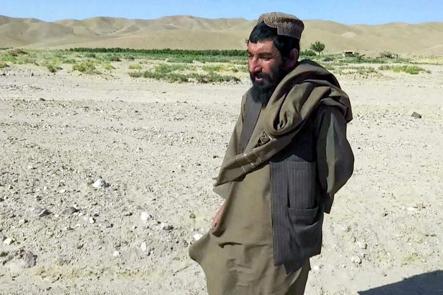 An Afghan man in traditional dress stands in a valley.