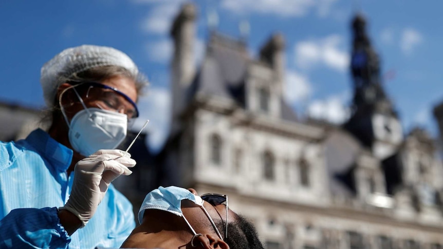 A health worker, wearing a protective suit and a face mask, prepares to administer a nasal swab to patient
