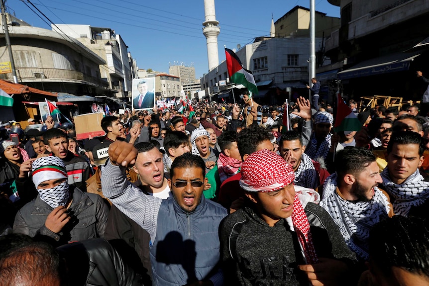 A group of protesters cram in a street in Jerusalem holding Palestinian flags and yelling chants.