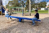 Two of pam's kids on either end of a seesaw, with one side up higher than the other. 
