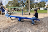 Two of pam's kids on either end of a seesaw, with one side up higher than the other. 