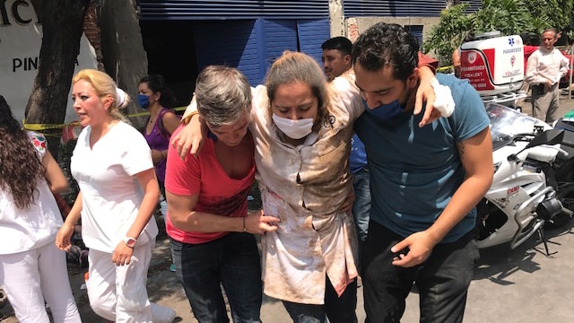 People help an injured person walk after an earthquake.