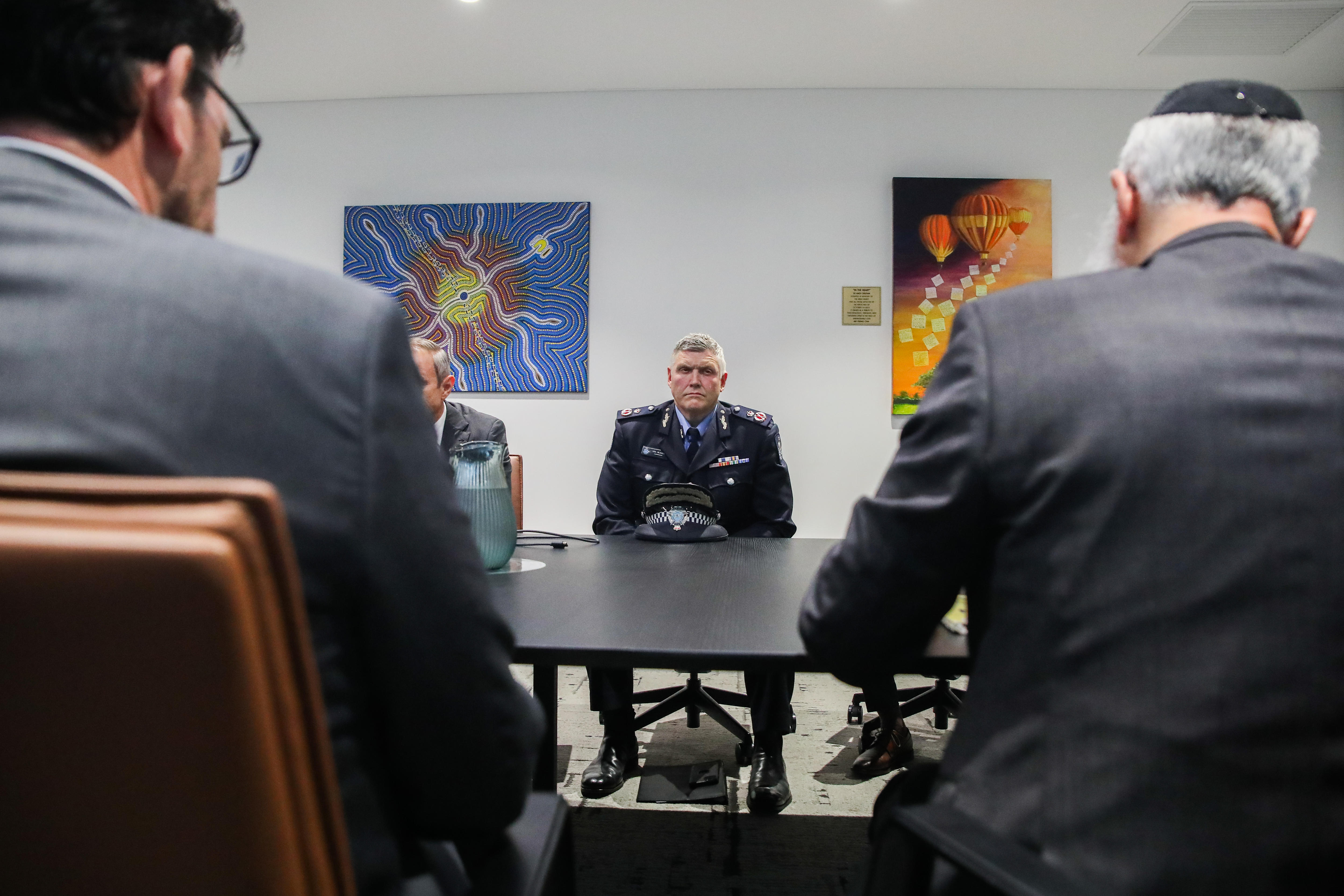 El comisionado de policía de WA, coronel Blanch, se sienta en una mesa grande durante una reunión con dos personas enfrentadas en primer plano.