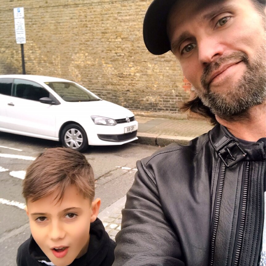 Father takes selfie with son on urban street.