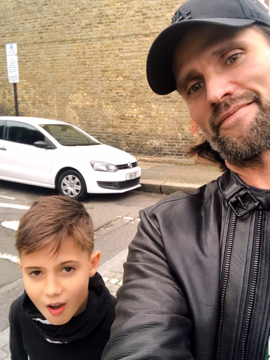 Father takes selfie with son on urban street.
