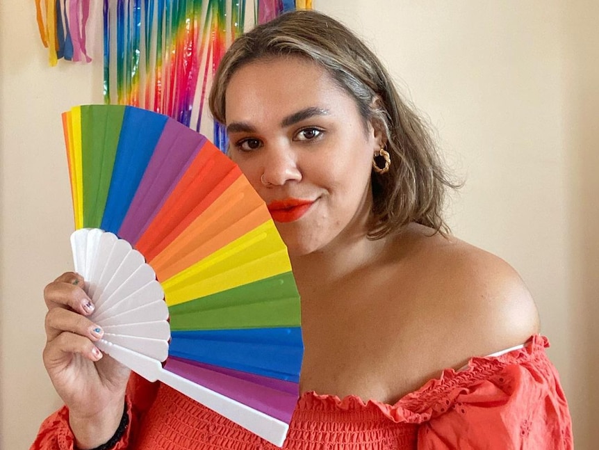 Allira holds a rainbow fan and smiles at the camera.