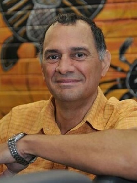 A man sitting in front of a wall with an Indigenous motif