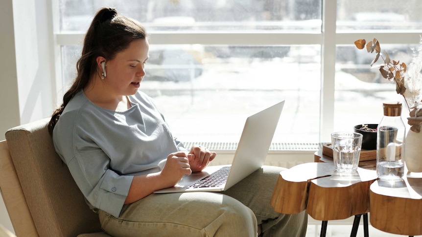 Young woman sits on sofa chair with laptop