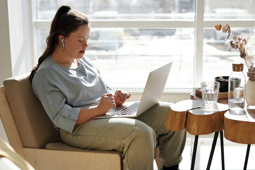 A woman with Downs Syndrome working at a laptop computer.