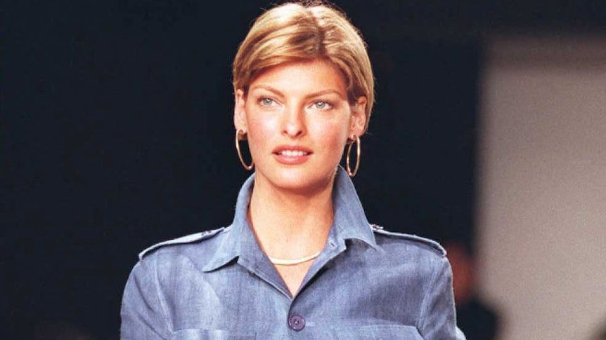 Model Linda Evangelista wears a blue jacket shirt over matching pants on the runway.