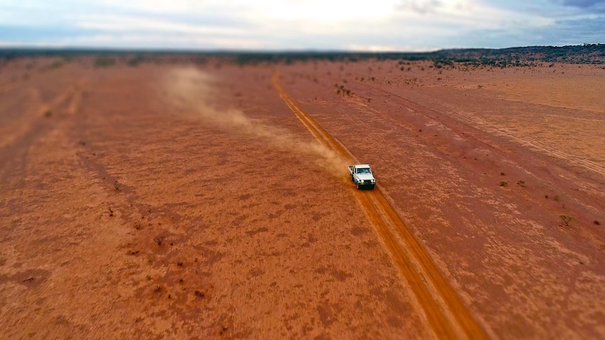 A ute drives across a barren paddock