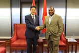 China's ambassador to PNG Xue Bing shakes hands with PNG Prime Minister James Marape in front of chairs and the PNG flag