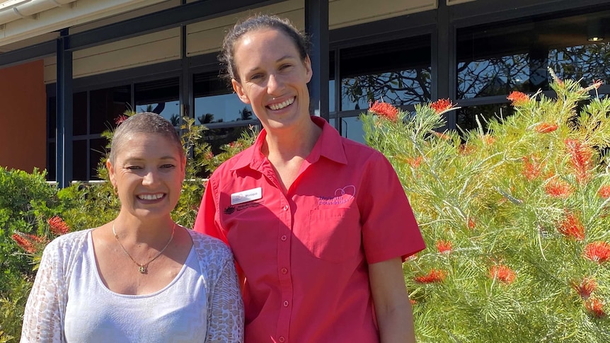 Two women smile in front of a flowering Grevillia