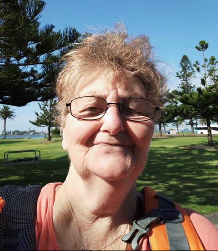 A woman wearing glasses smiling while standing in a park. 