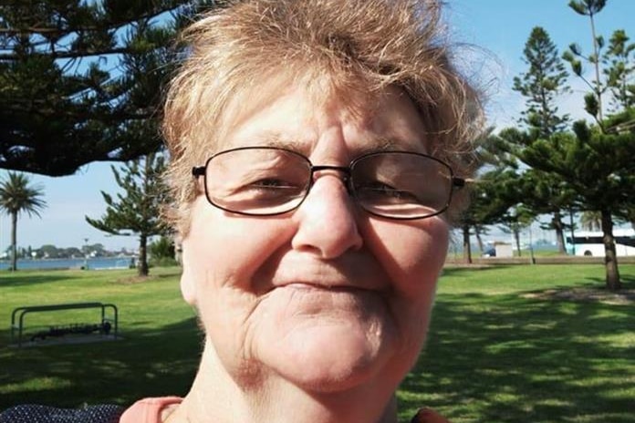 A woman wearing glasses smiling while standing in a park. 