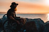 Man sits in a wheelchair at a beach at sunset