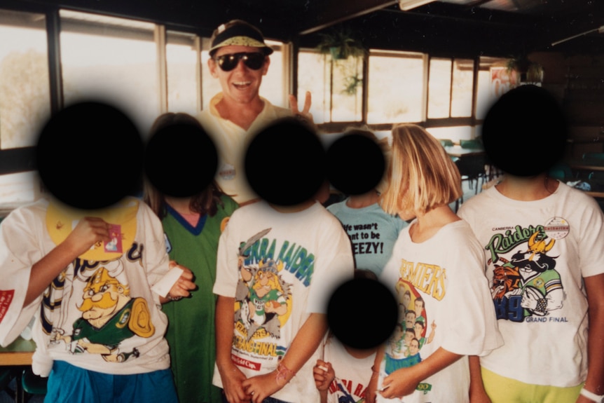 An old photo of a smiling man wearing sunglasses and giving a V sign, behind several young people with blurred faces.