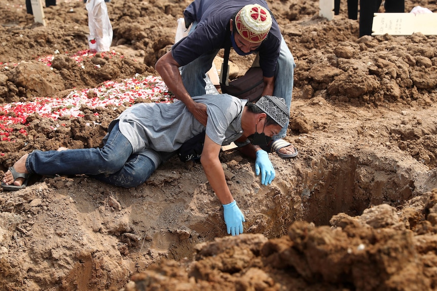 A man falls on the ground as he weeps during the burial of a relative