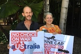 A man and woman standing under a tree holding Pine Gap protest signs