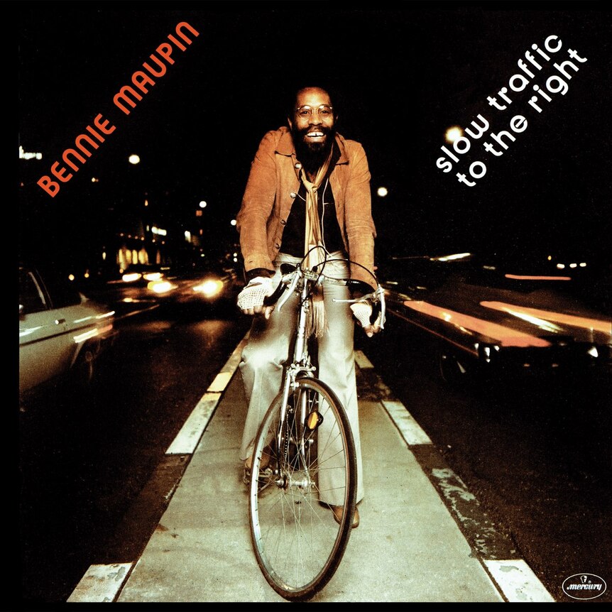 A young Bennie Maupin riding his bike up the middle lane of traffic as cars pass by on either side