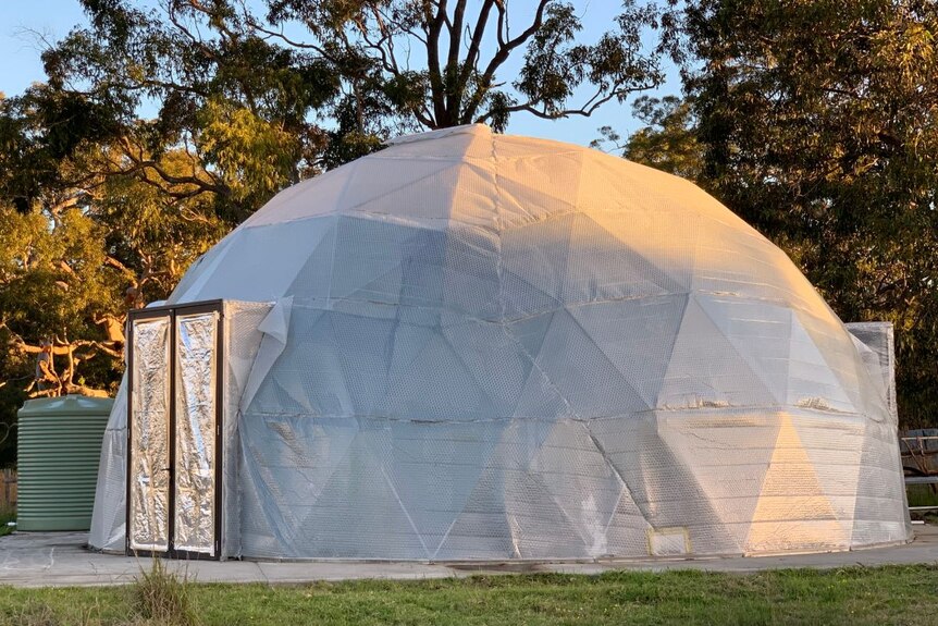 A canvas dome on a lawn, with a metallic door inside.