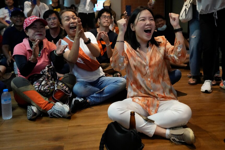 Women cheering wearing orange while sitting on floor.