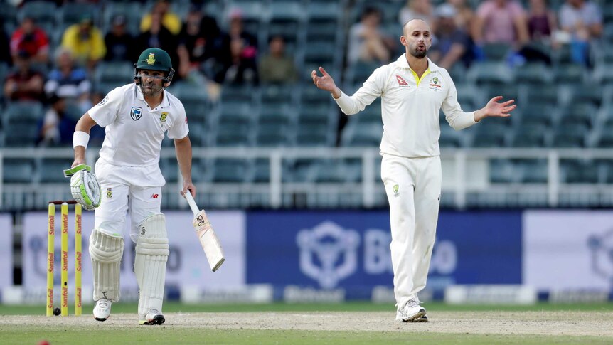 Nathan Lyon stands with his arms out, next to batsman Dean Elgar during a cricket match.
