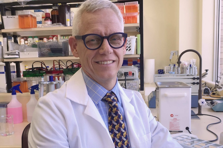 UWA associate professor Craig Pennell sits at a chair in a lab wearing a white lab coat.