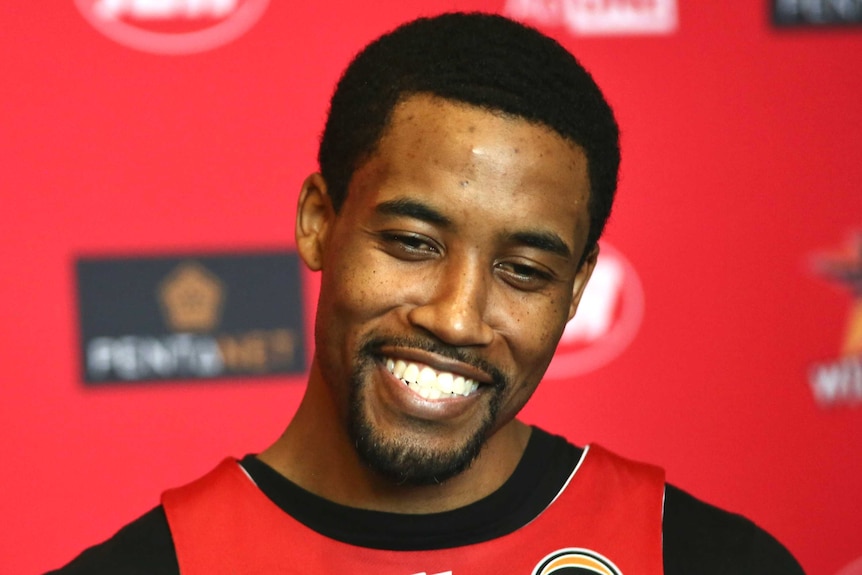 Perth Wildcats Bryce Cotton smiling in front of a red background