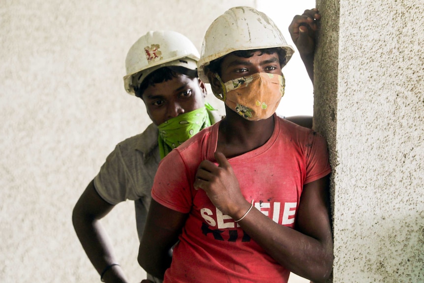 Two construction workers in hard hats lean against a wall