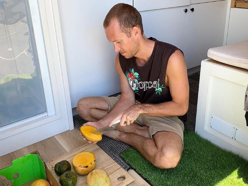 Man sits on the floor of a van chopping up fruit.