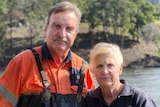 a man in overalls and a woman standing in front of river smiling