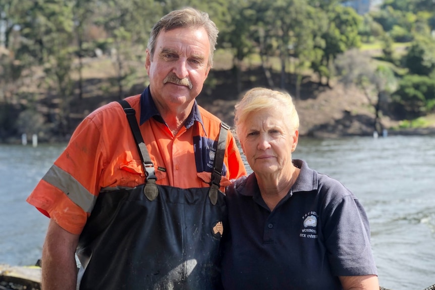 a man in overalls and a woman standing in front of river smiling