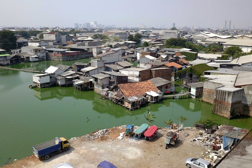 A drone shot showing a village surrounded by green, stagnant water