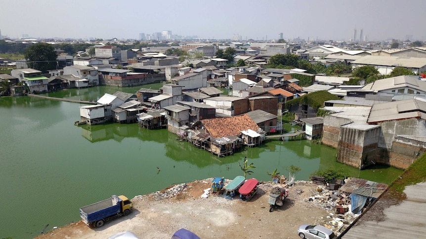 A drone shot showing a village surrounded by green, stagnant water