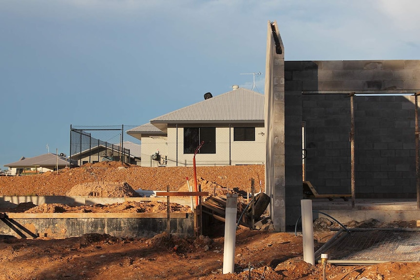 A front-on view of a new house being built while a completed one stands behind it.