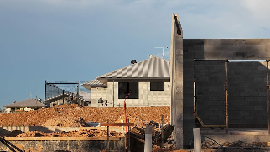 A front-on view of a new house being built while a completed one stands behind it.