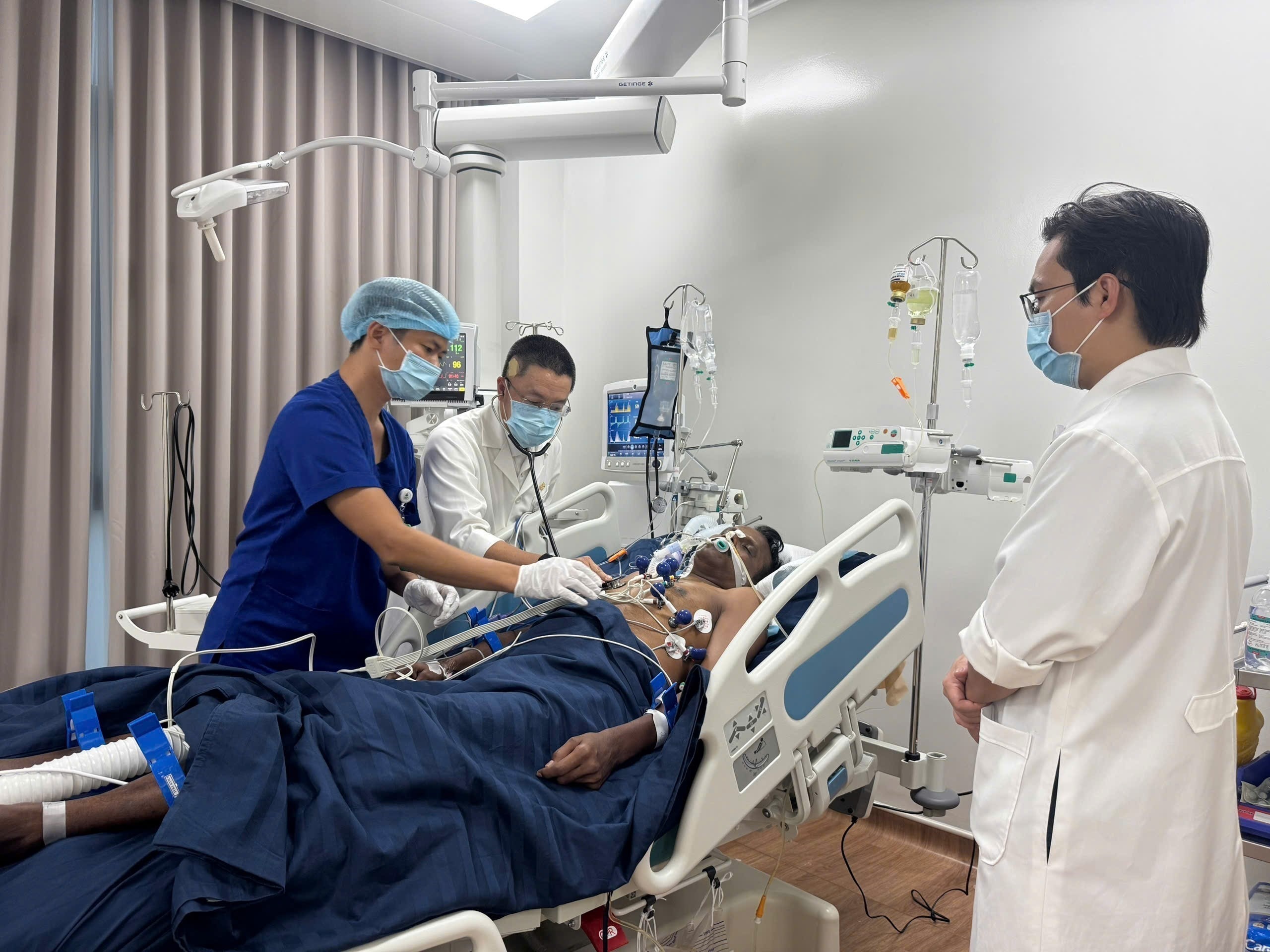 An Indian tourist is receiving treatment in a hospital bed, surrounded by three medical staff wearing face masks.