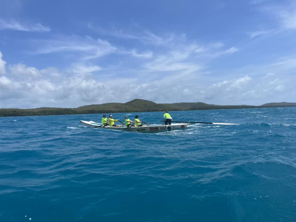 A group of men row a surf boat across an open body of water