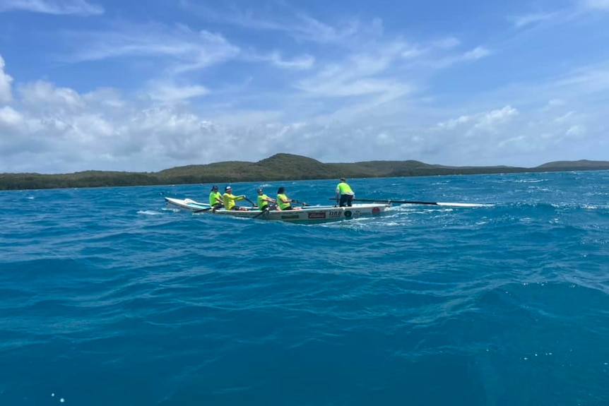 A group of men row a surf boat across an open body of water
