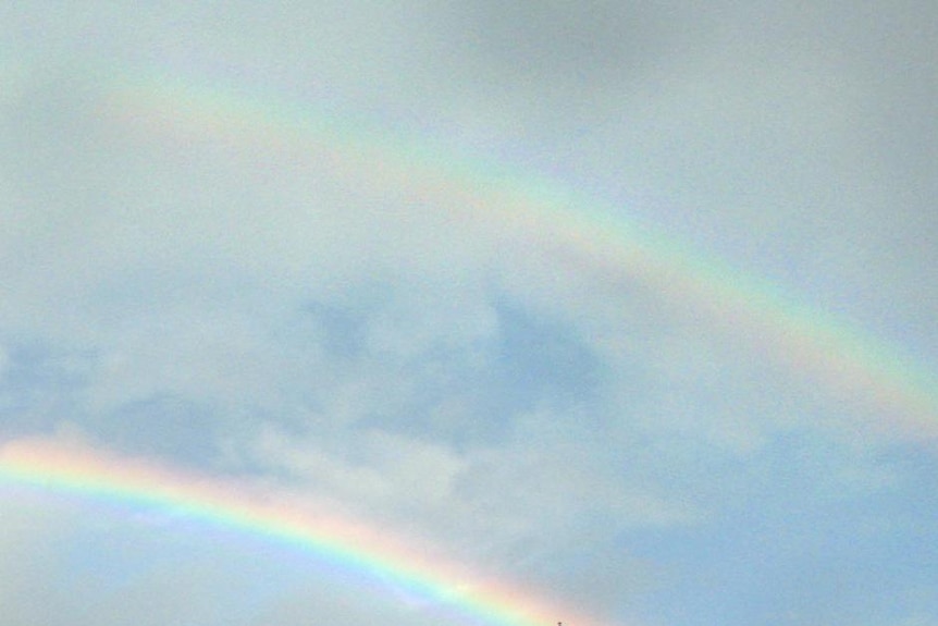 An old-style ship on the sea with a rainbow overhead.