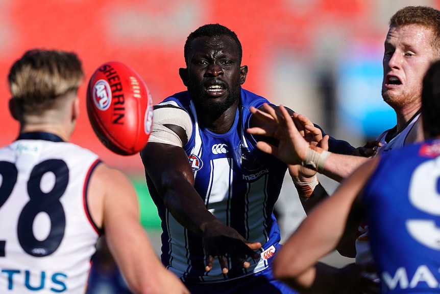 A North Melbourne AFL player watches the ball in front of him while surrounded by a teammate and an Adelaide opponent.