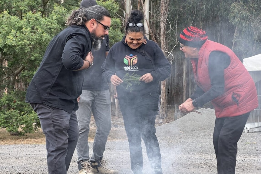 A group of smiling Indigenous people perform a smoking ceremony.