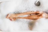 A woman's legs and feet, with red toenails, showing through the bubbles in a bath