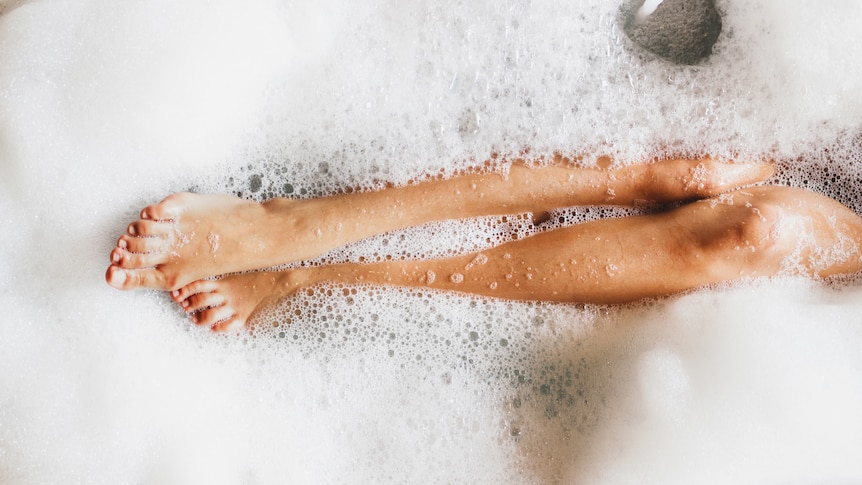 A woman's legs and feet, with red toenails, showing through the bubbles in a bath