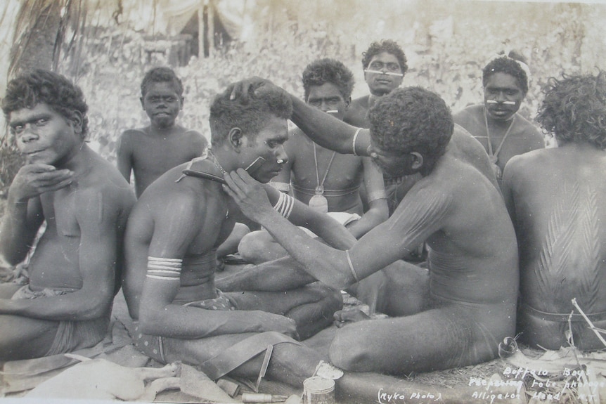 Young Aboriginal men shaving with a blade.
