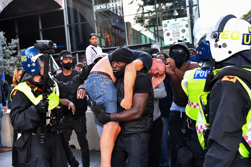 A black man carries an injured white counter-protester to safety over his shoulder.