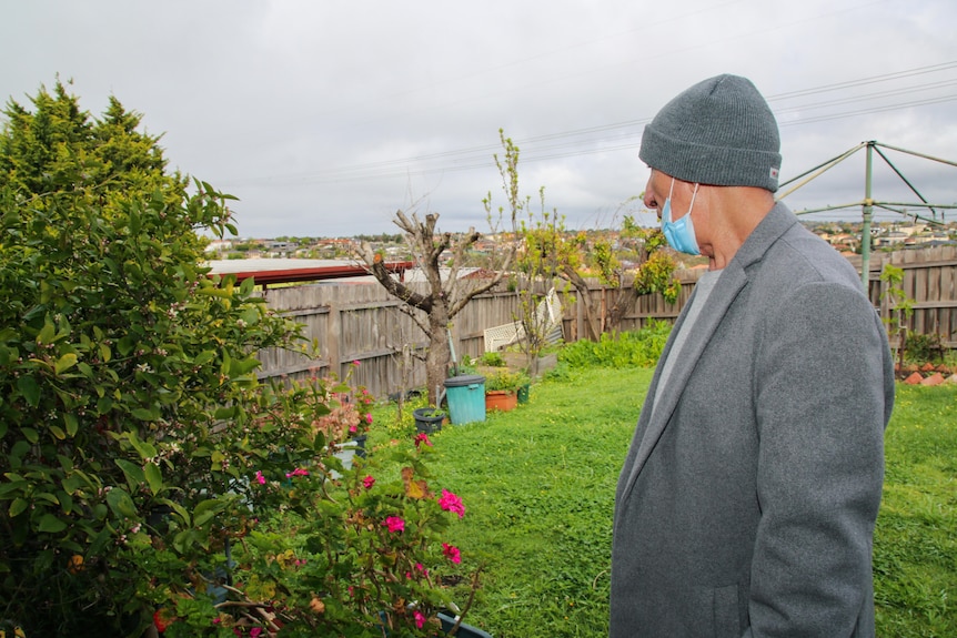 Shaker Sako stands in his backyard with a clothesline and green row of plants.