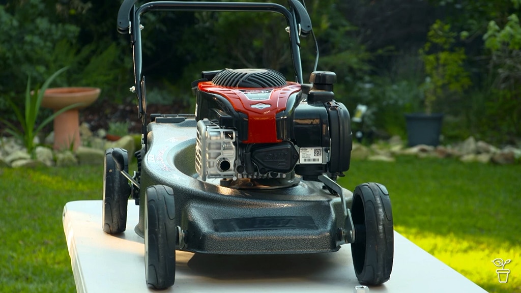 A petrol lawnmower on a table in a garden.